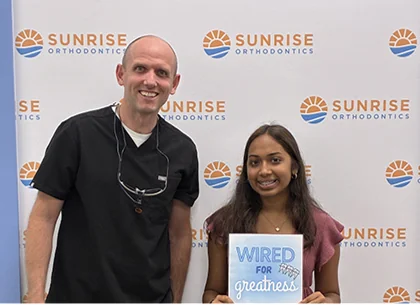 Smiling teen with braces holding a Wired for Greatness sign beside Dr. Steven Dent